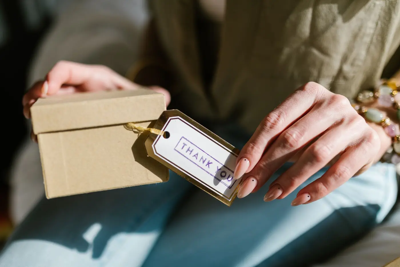 Hands holding a gift box with a thank-you card