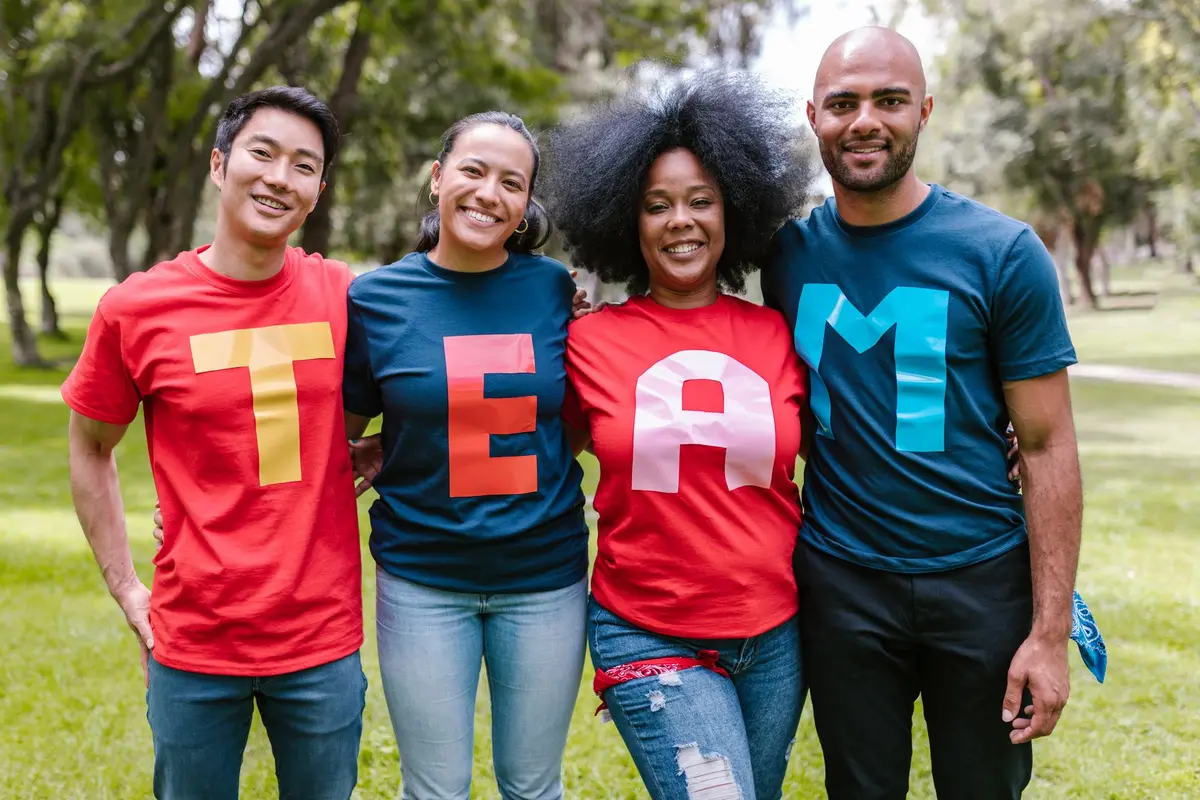 Four smiling friends in colorful matching shirts that spell TEAM