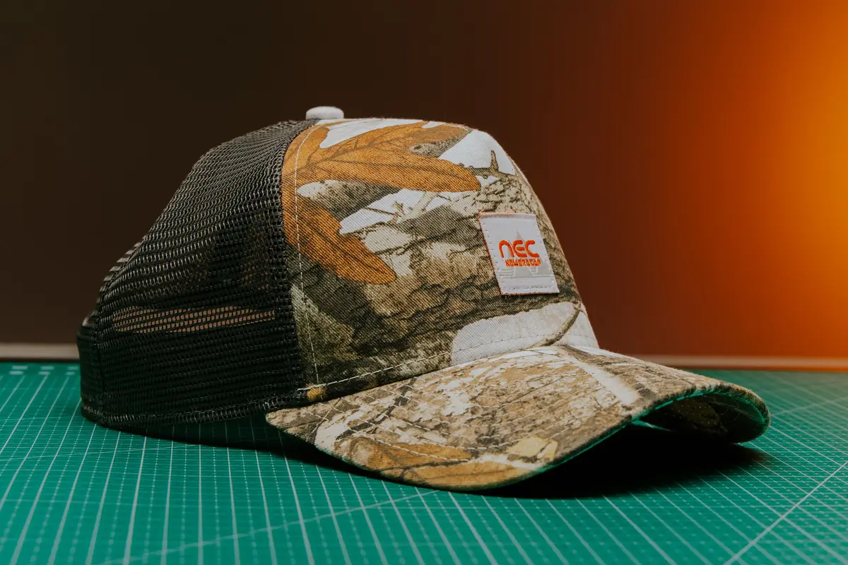 A camo trucker hat with a mesh back and a small logo patch on a cutting mat
