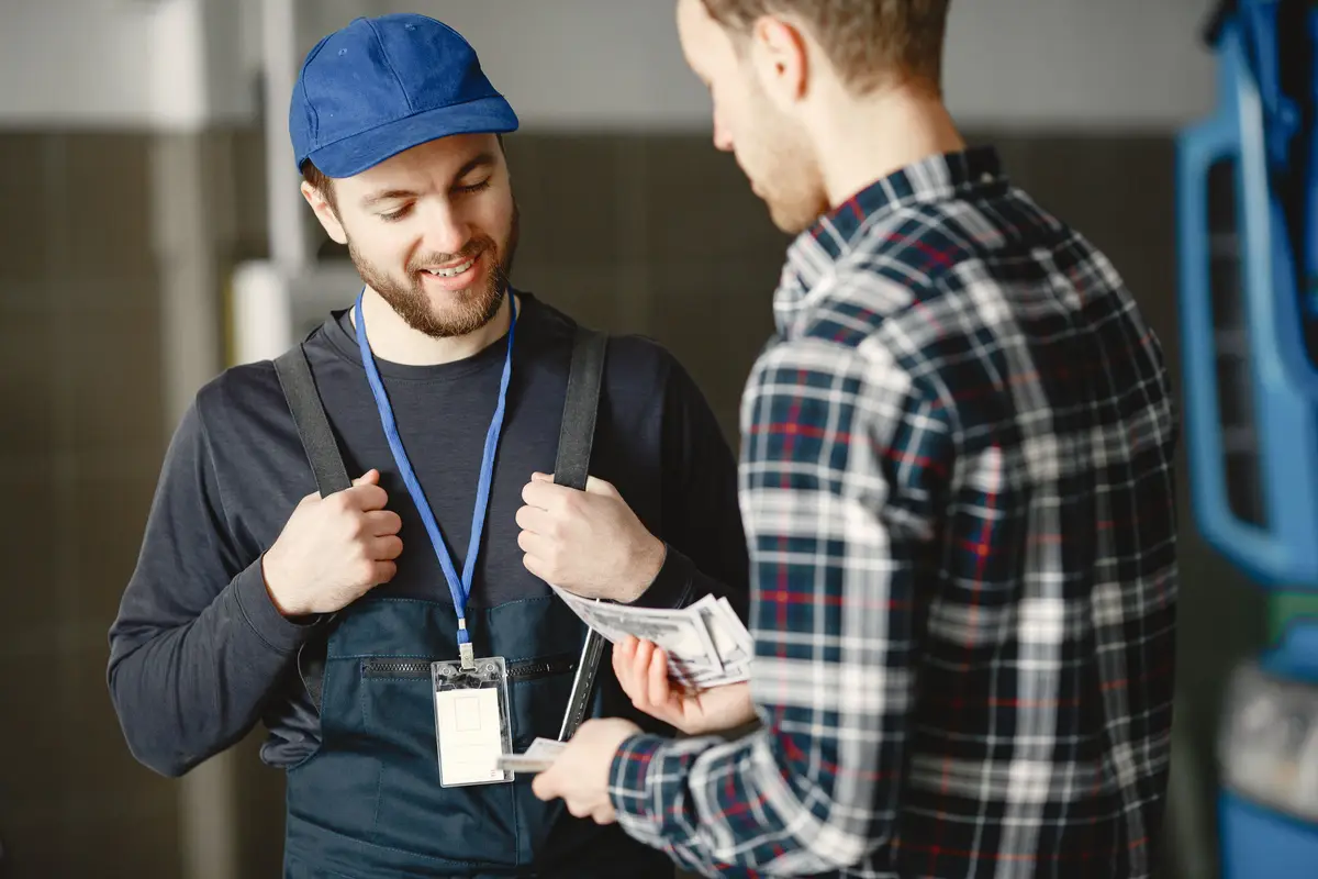 A smiling worker in a blue cap and overalls talking with a customer
