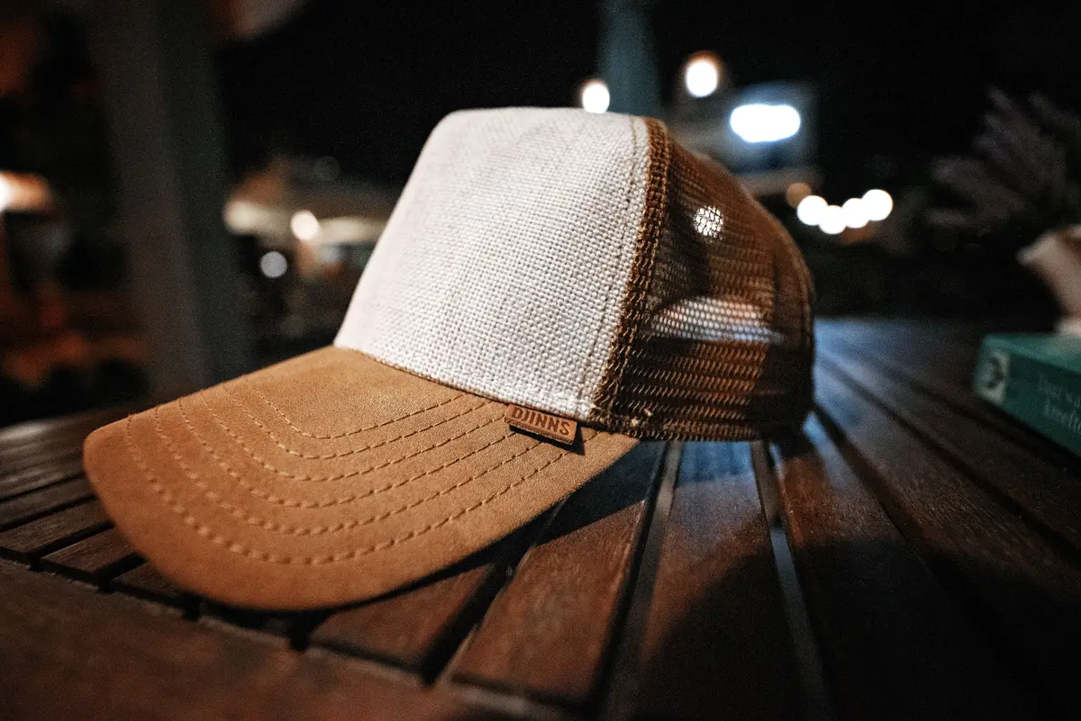 A mesh-back trucker hat with a tan front panel resting on a wooden table