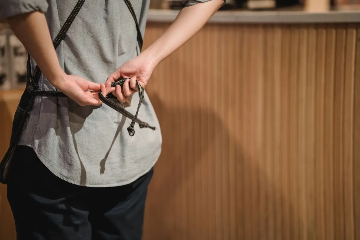 A barista tying the strap of a canvas apron before a shift