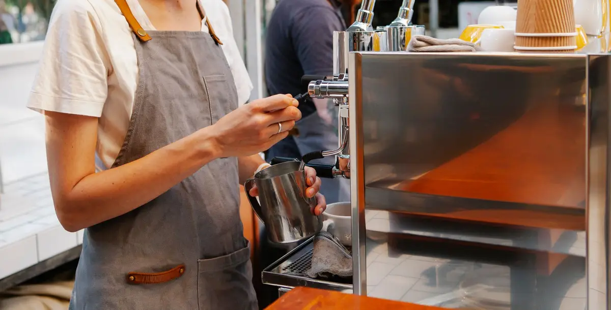 A barista in an apron preparing coffee at an espresso machine