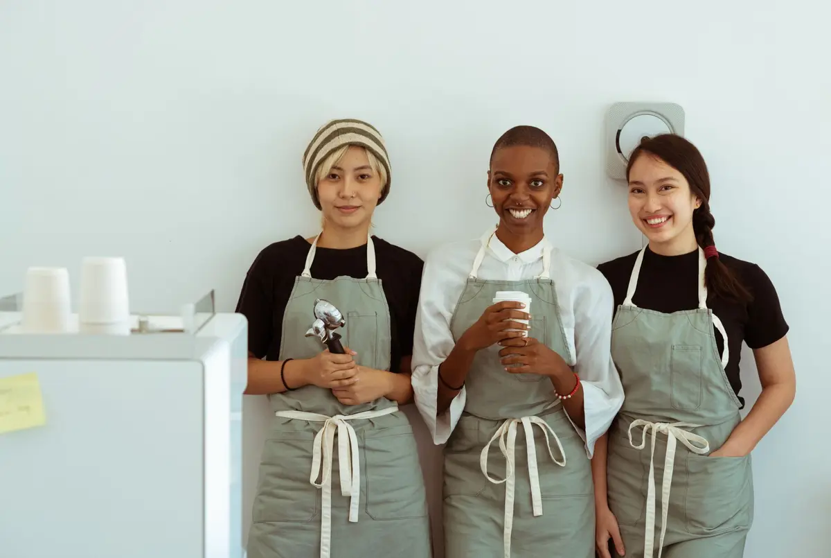 Three baristas in matching gray aprons standing together behind a café counter