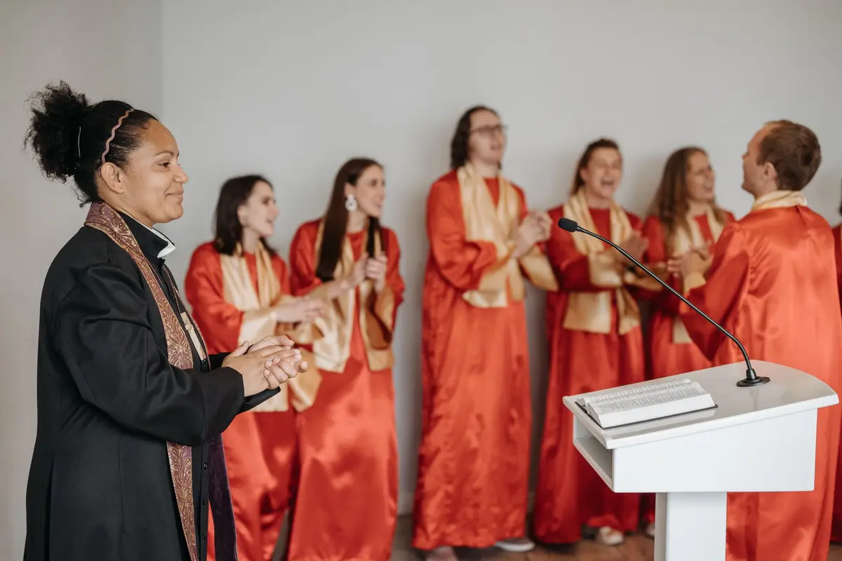 A choir in red robes clapping and singing while a pastor leads them