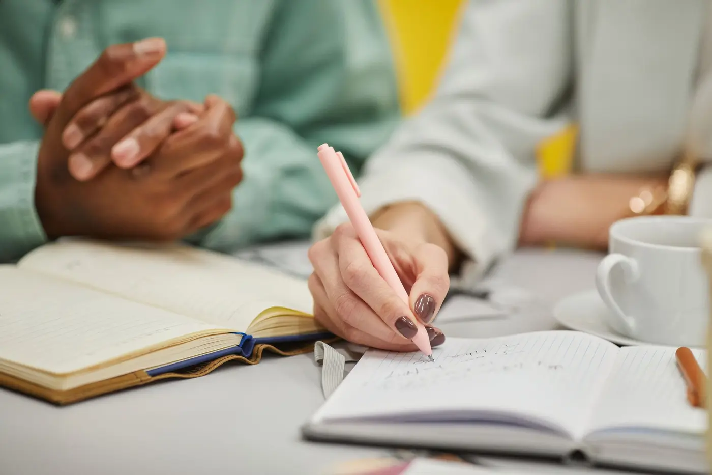 Hands writing plans and numbers in a notebook on a desk