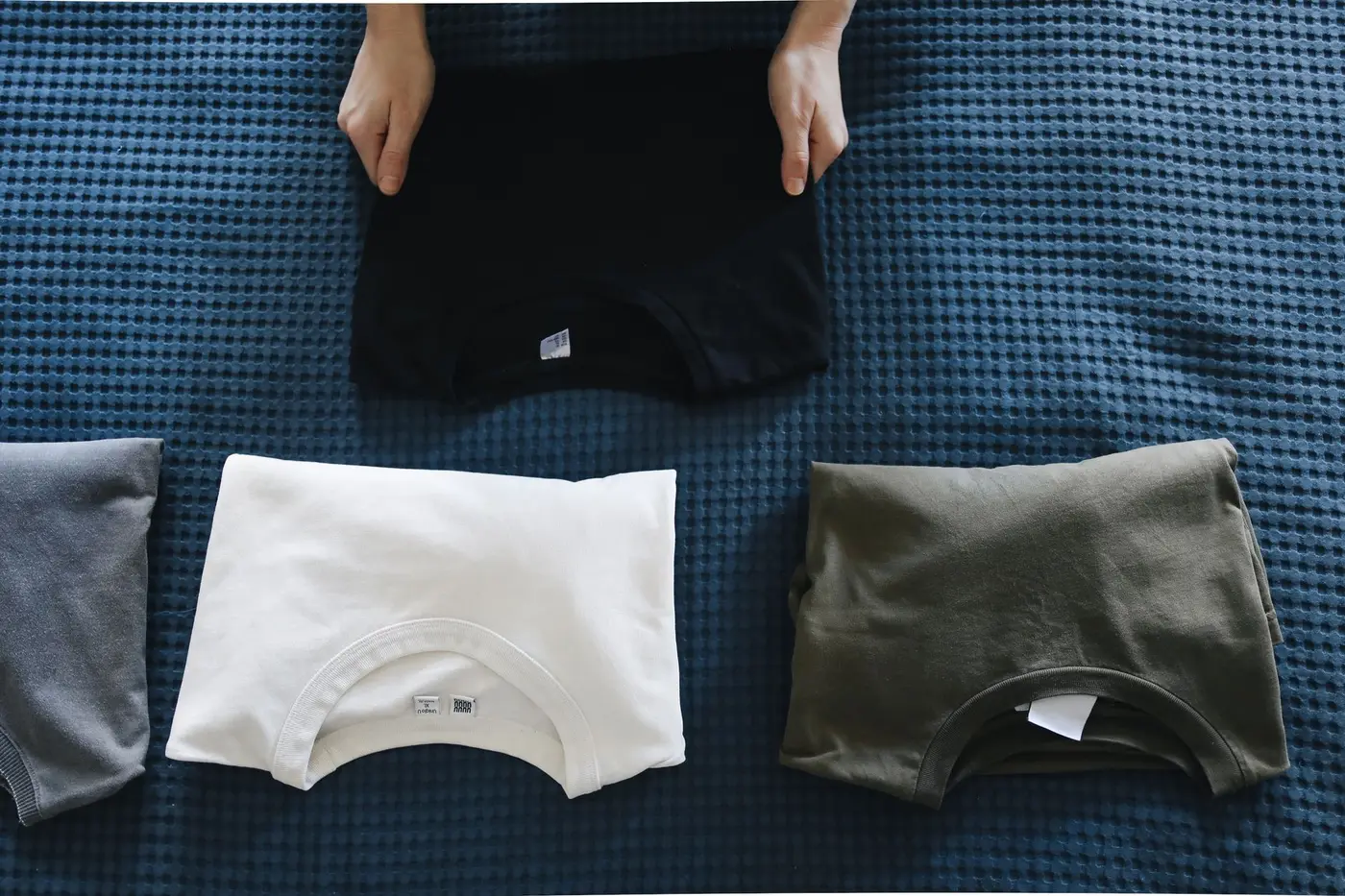 Neatly folded custom church t-shirts in black, white, and olive laid out on a table