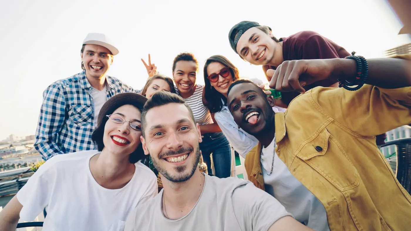 A happy, diverse group of young adults taking a group selfie outdoors