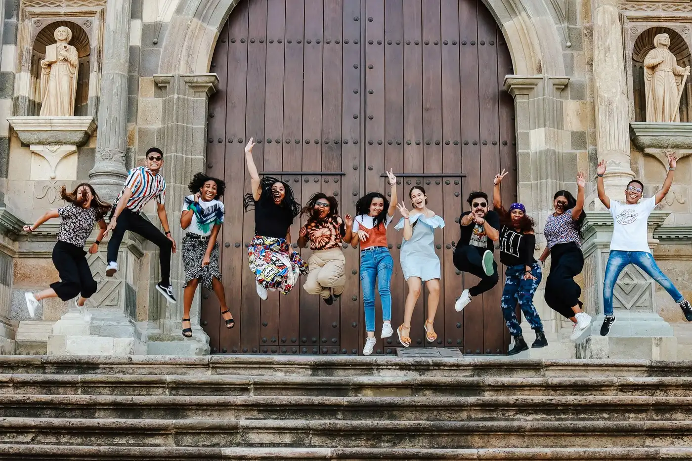 A group of friends jumping joyfully on the steps outside a cathedral