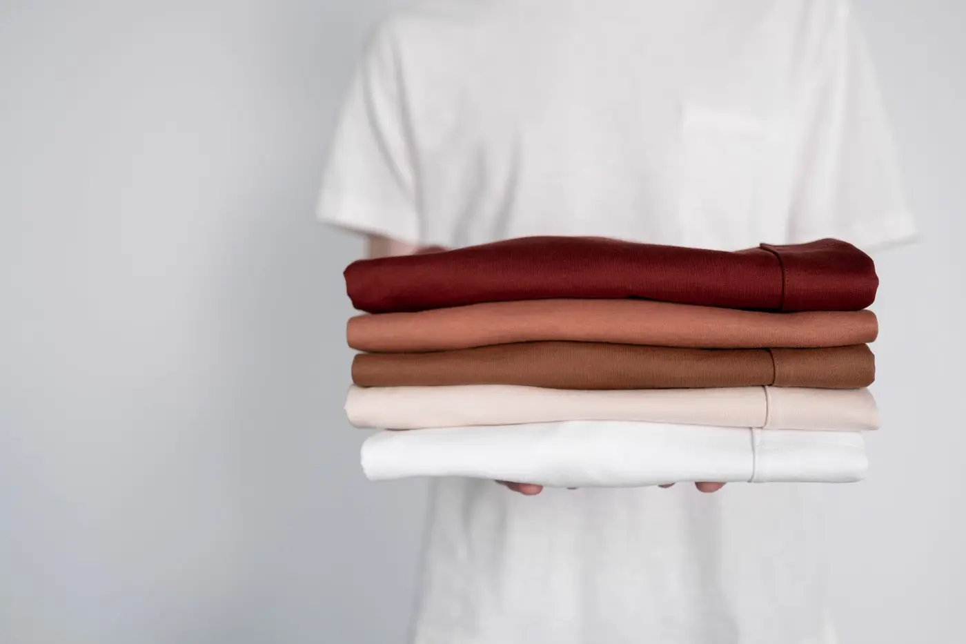 A stack of neatly folded t-shirts in cream, rust, and burgundy