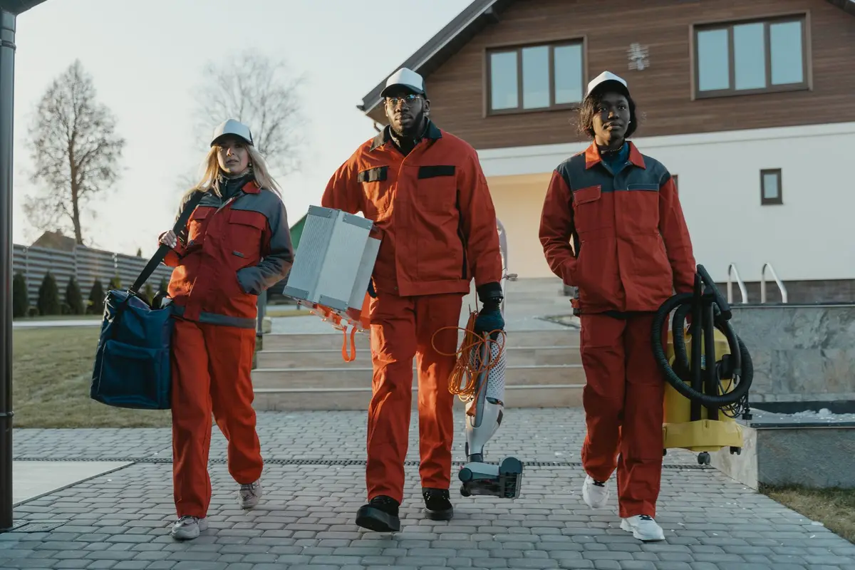 A cleaning crew in matching orange uniforms arriving at a house with their equipment