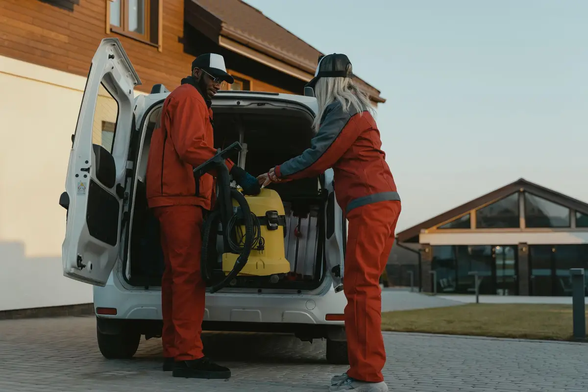 Two cleaners in matching uniforms loading equipment into a company van