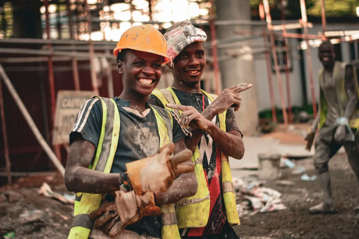 Two smiling construction workers in hard hats and hi-vis safety vests on a job site