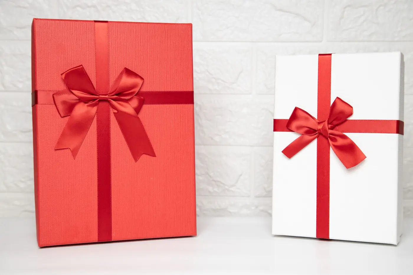 Two elegant corporate gift boxes with red ribbons on a white background