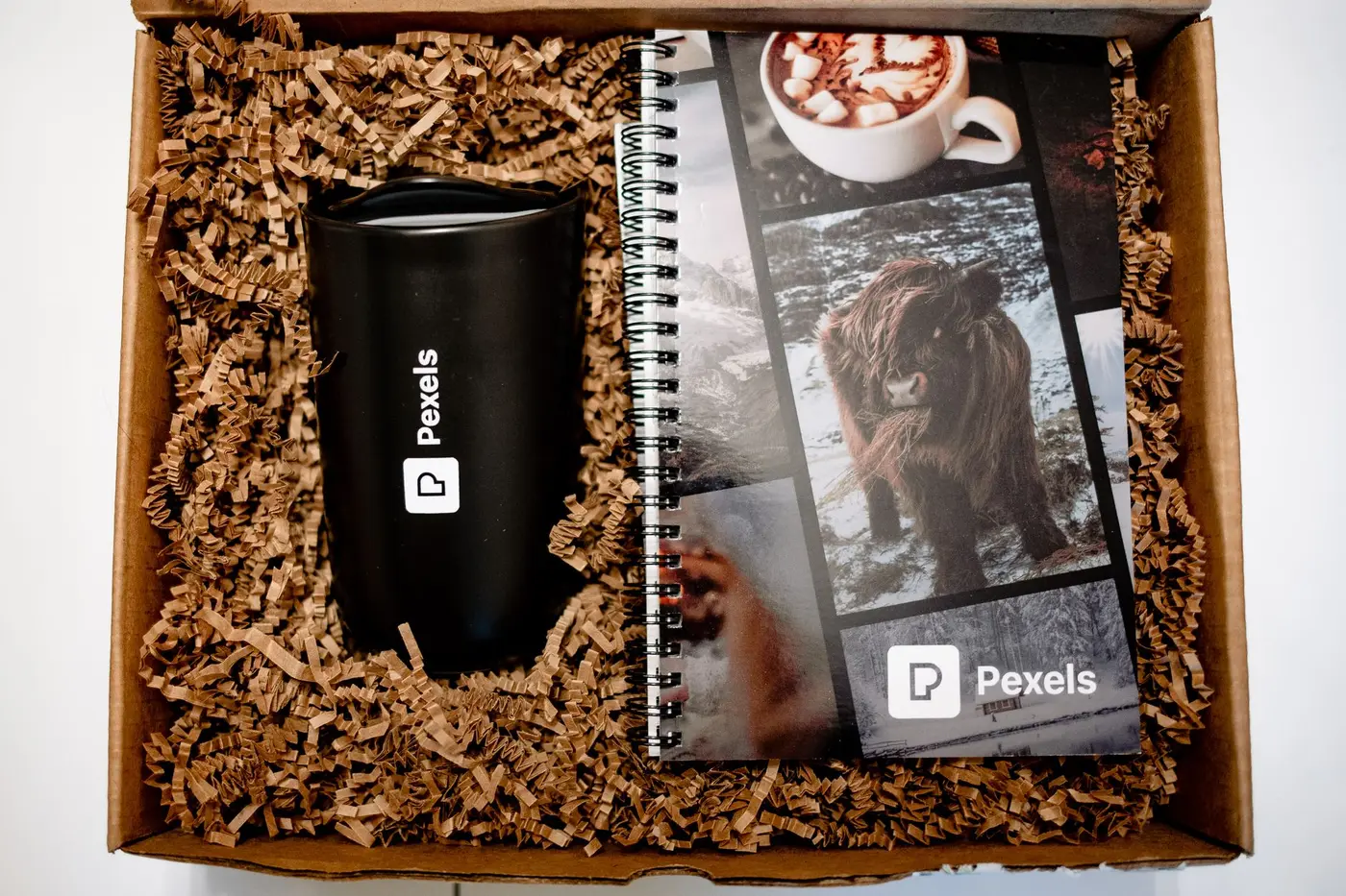 A branded black tumbler and notebook in a kraft gift box with shredded paper