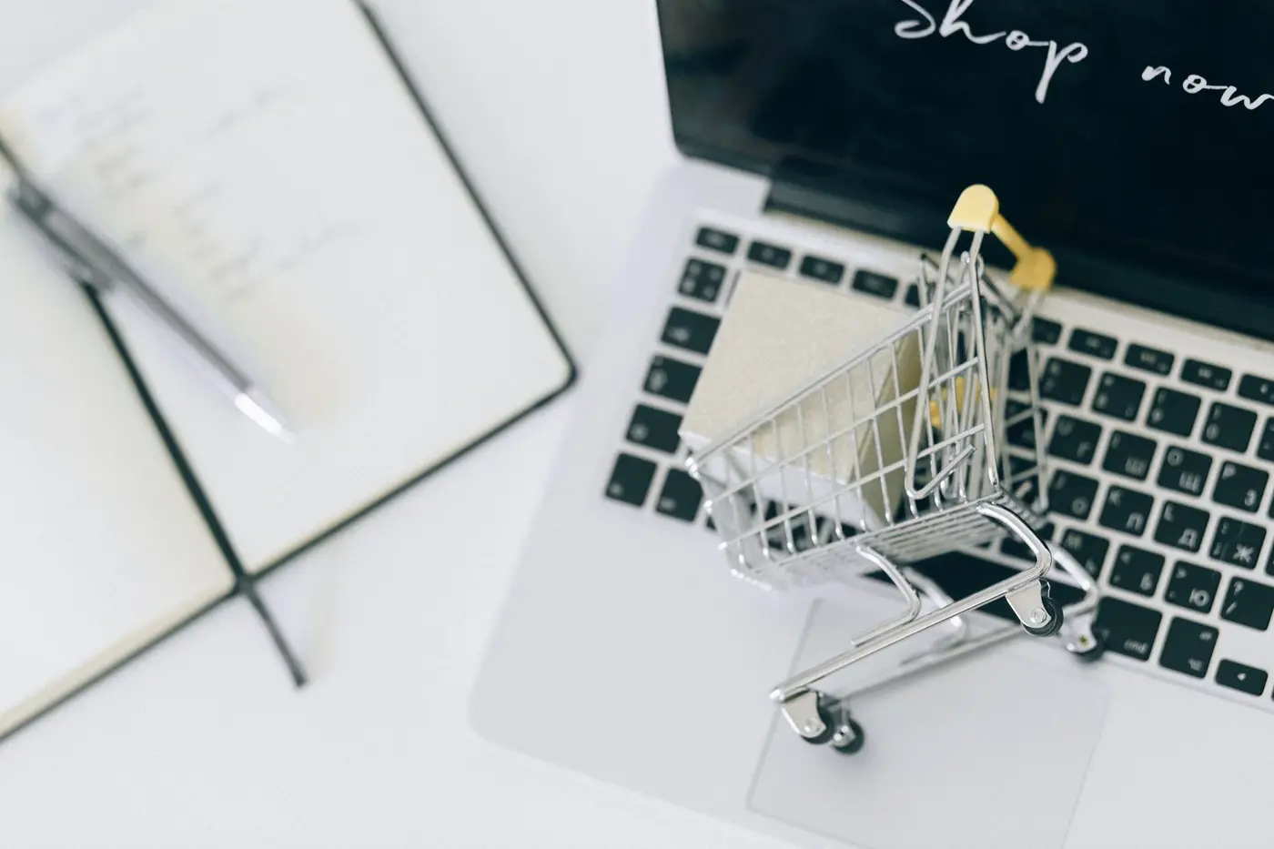 A small shopping cart beside a notepad and laptop