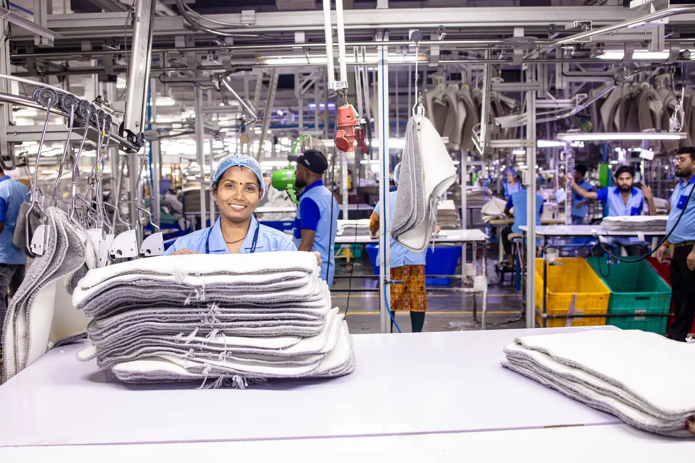 A worker in a textile production facility with stacks of folded garments