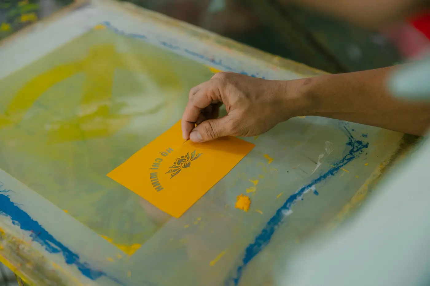 A hand pulling ink across a screen printing frame