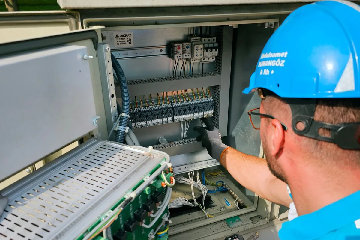 An electrician in work gear servicing an outdoor electrical panel