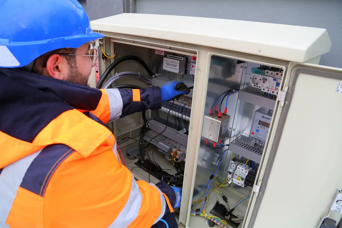 An electrician in safety gear working on an outdoor electrical panel