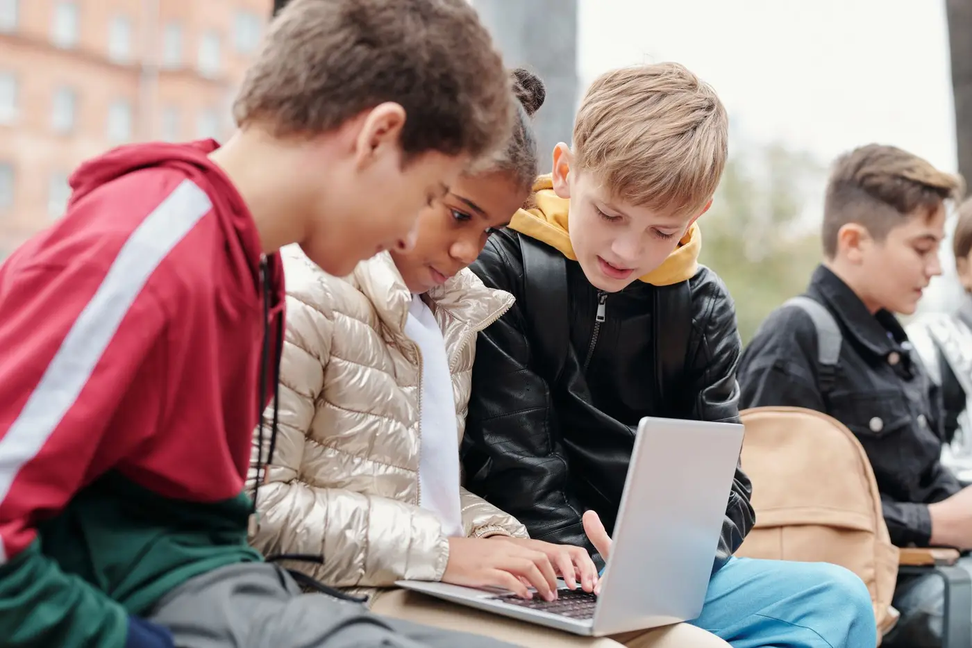 A group of teenagers gathered around a laptop outdoors