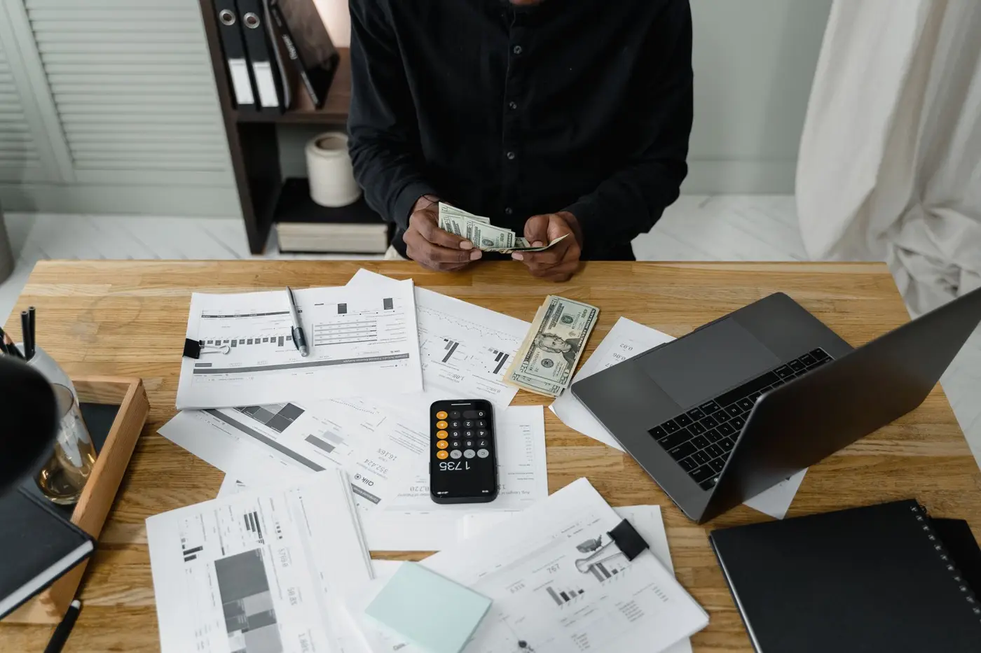 A person counting cash at a desk with a calculator and paperwork