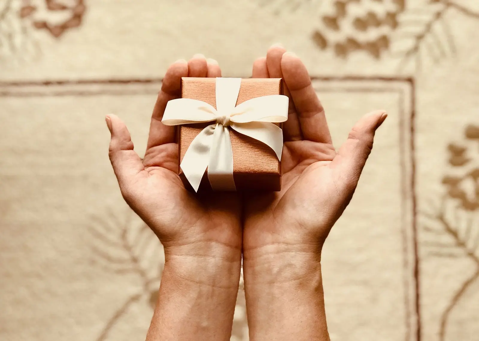 Hands presenting a small wrapped corporate gift to a client
