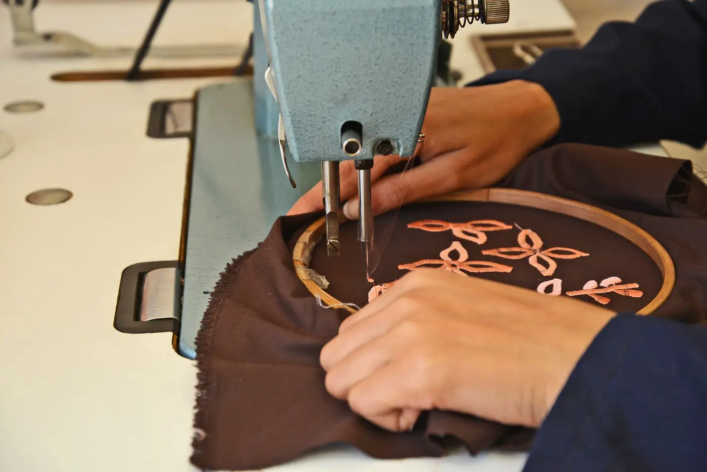 Hands guiding fabric through an embroidery machine in a workshop