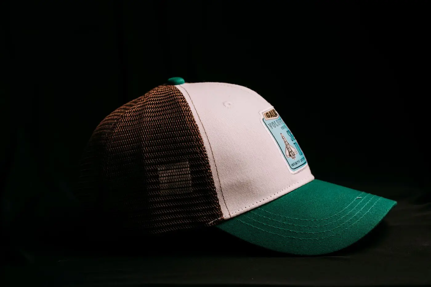A green and brown trucker hat with a woven patch on the front