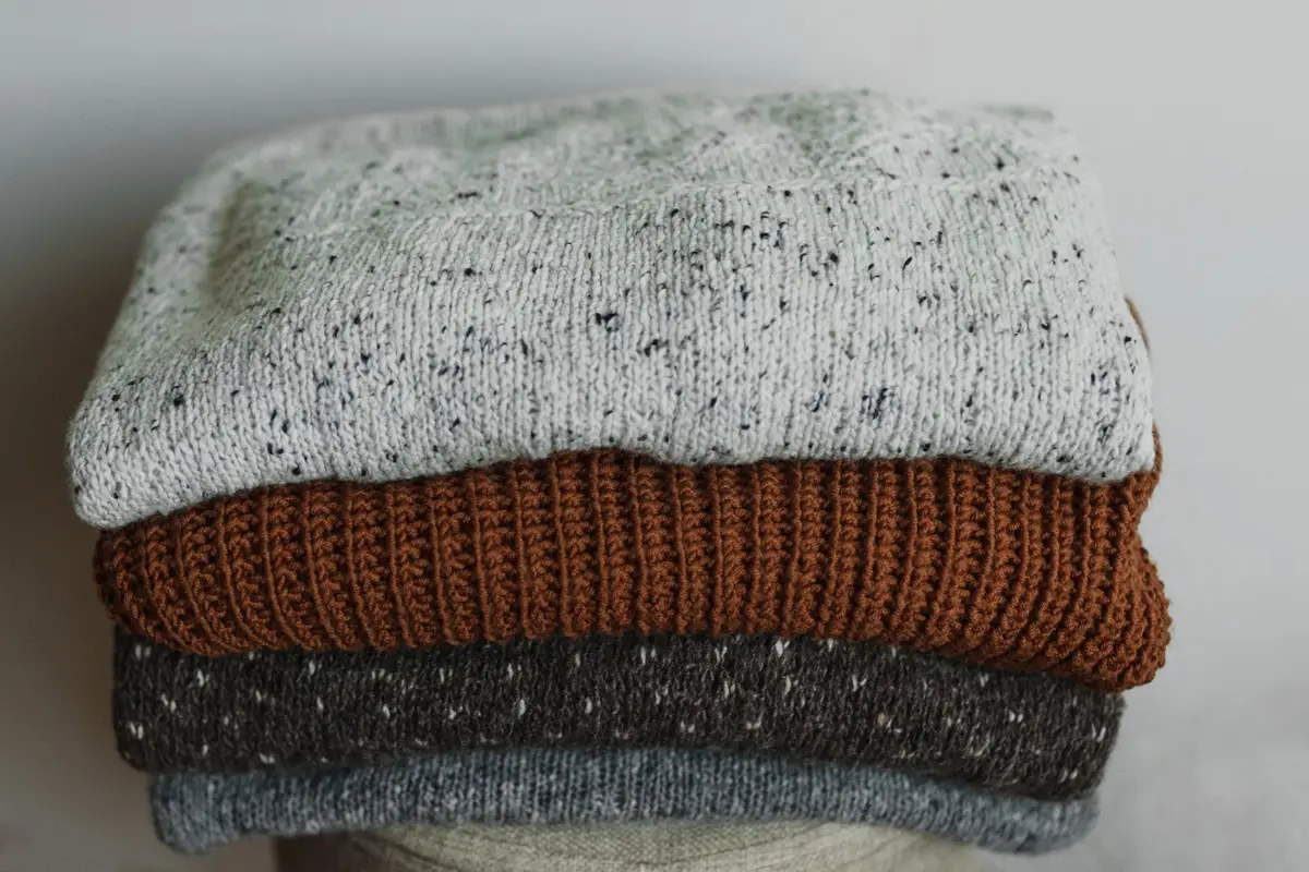 A neat stack of folded knit sweaters in neutral tones
