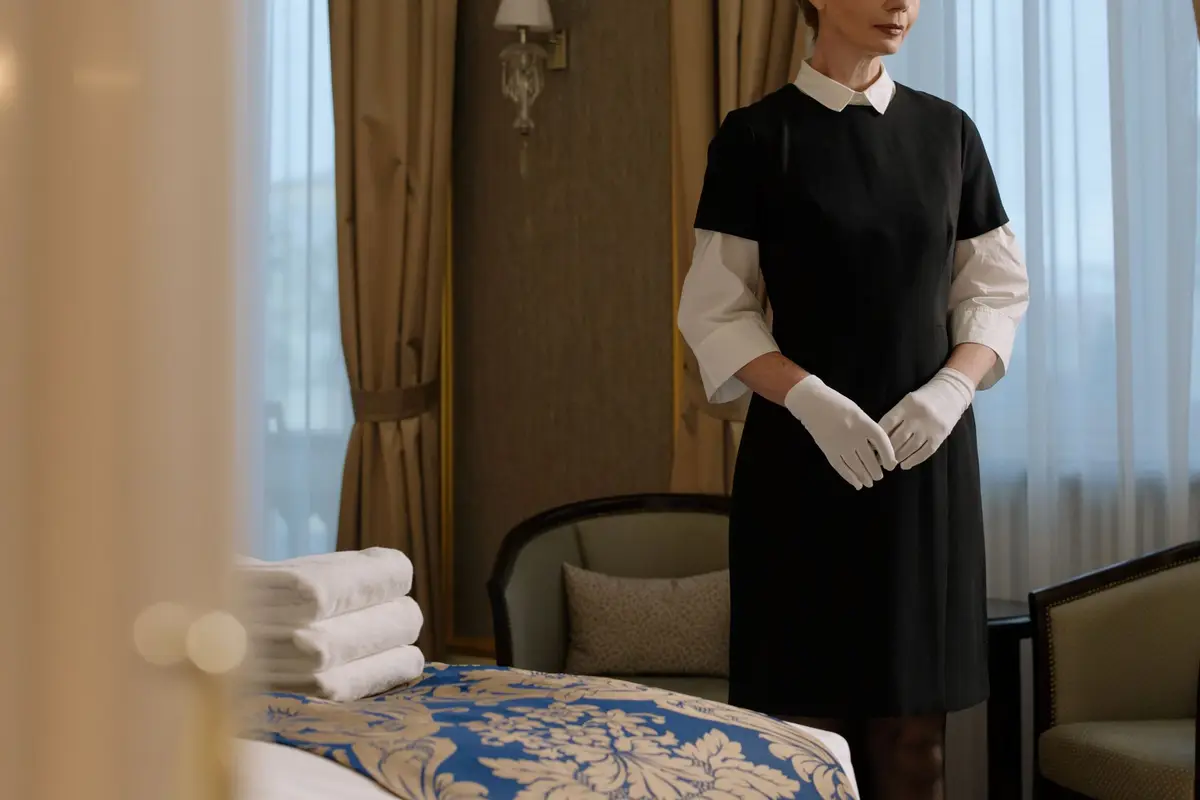 A hotel housekeeper in a classic black and white uniform preparing a guest room