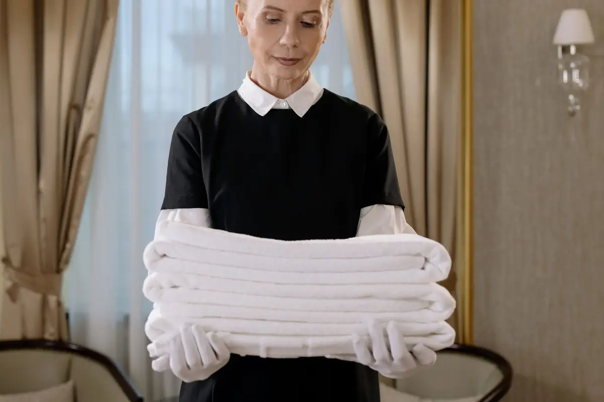 A housekeeper in uniform holding a stack of fresh white towels