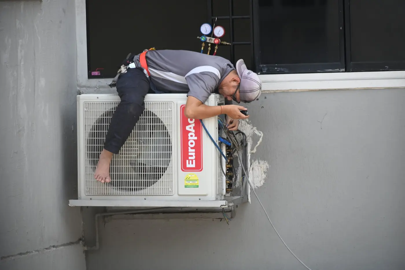 A technician working on an air conditioning unit mounted on a building wall