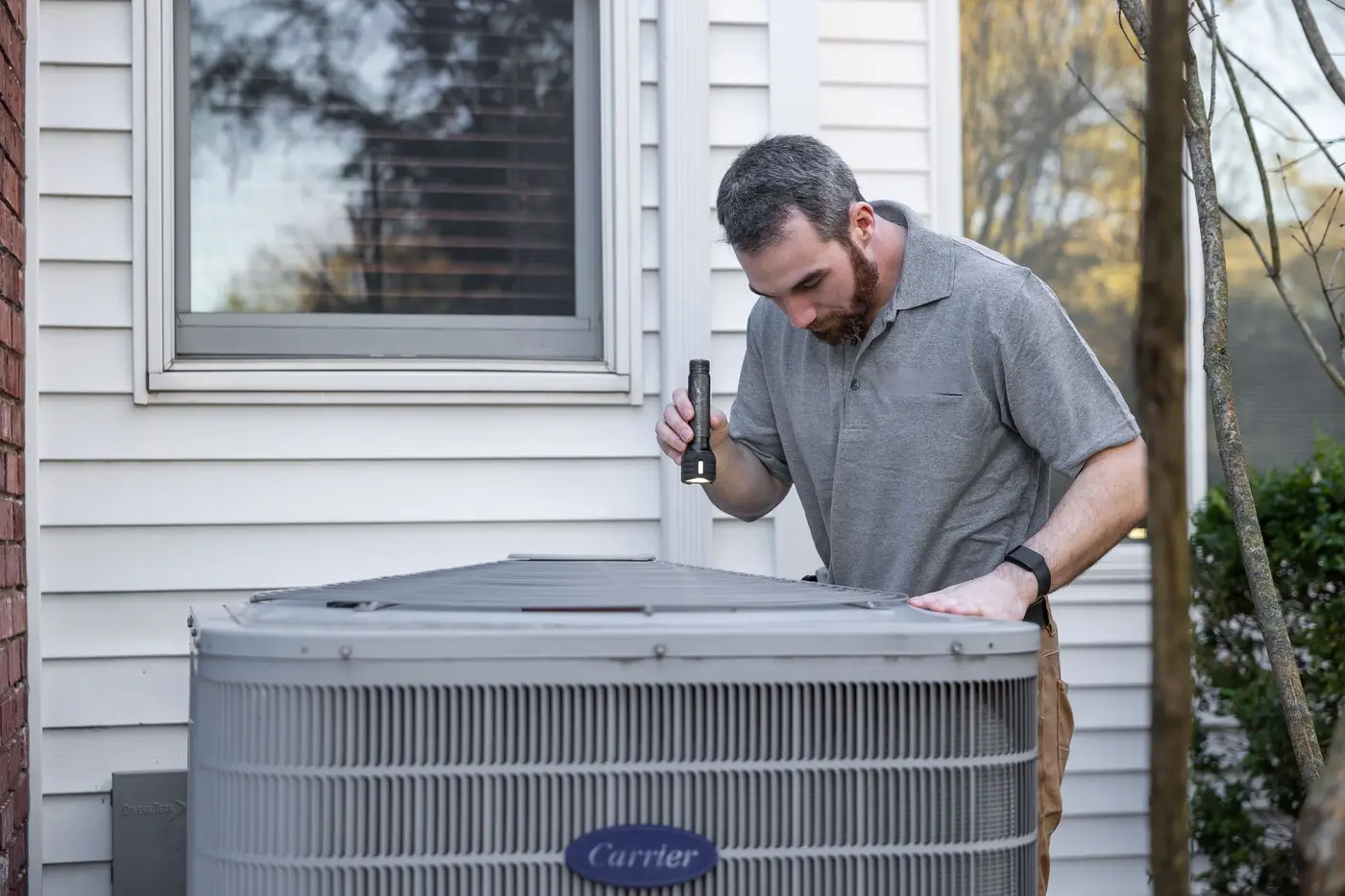 An HVAC technician inspecting an outdoor condenser unit at a home