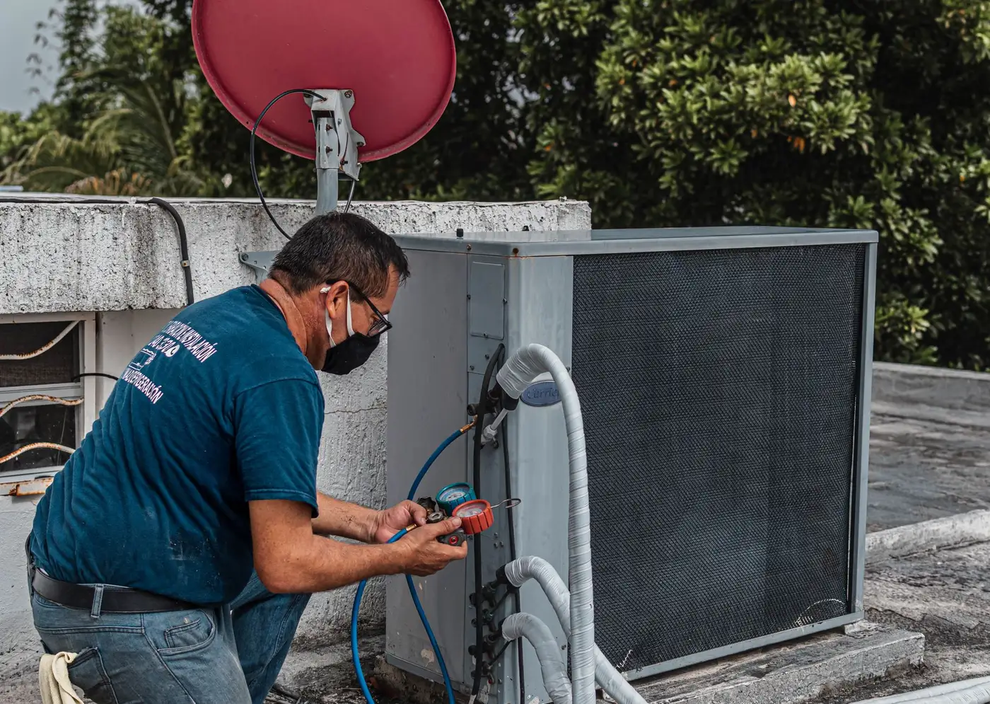 A technician using a manifold gauge to service an outdoor air conditioner