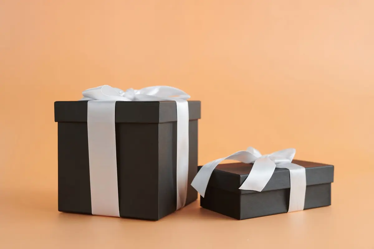 Two matte black gift boxes tied with white ribbons on a peach background