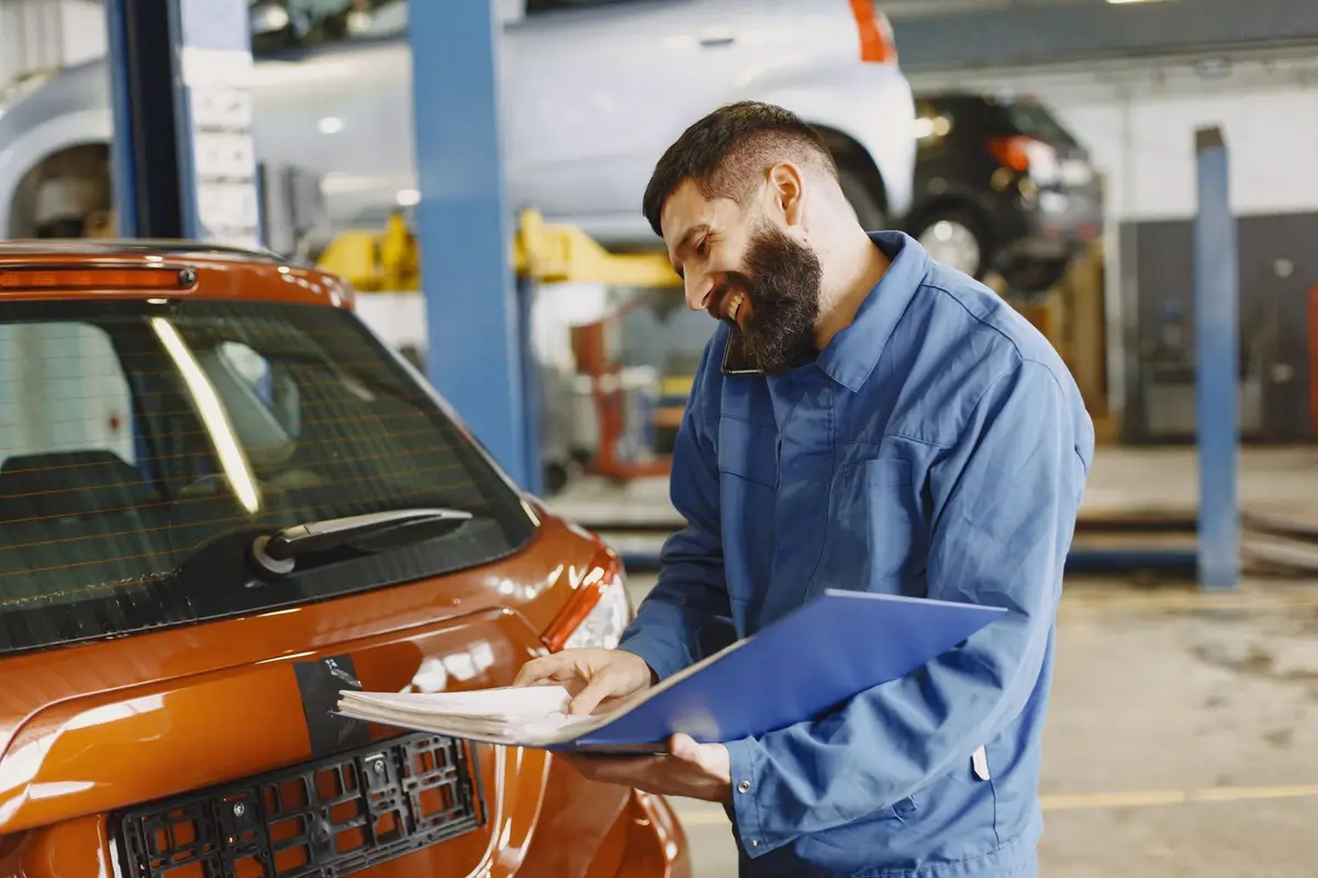A mechanic in a work shirt checking a repair order on a clipboard beside a car