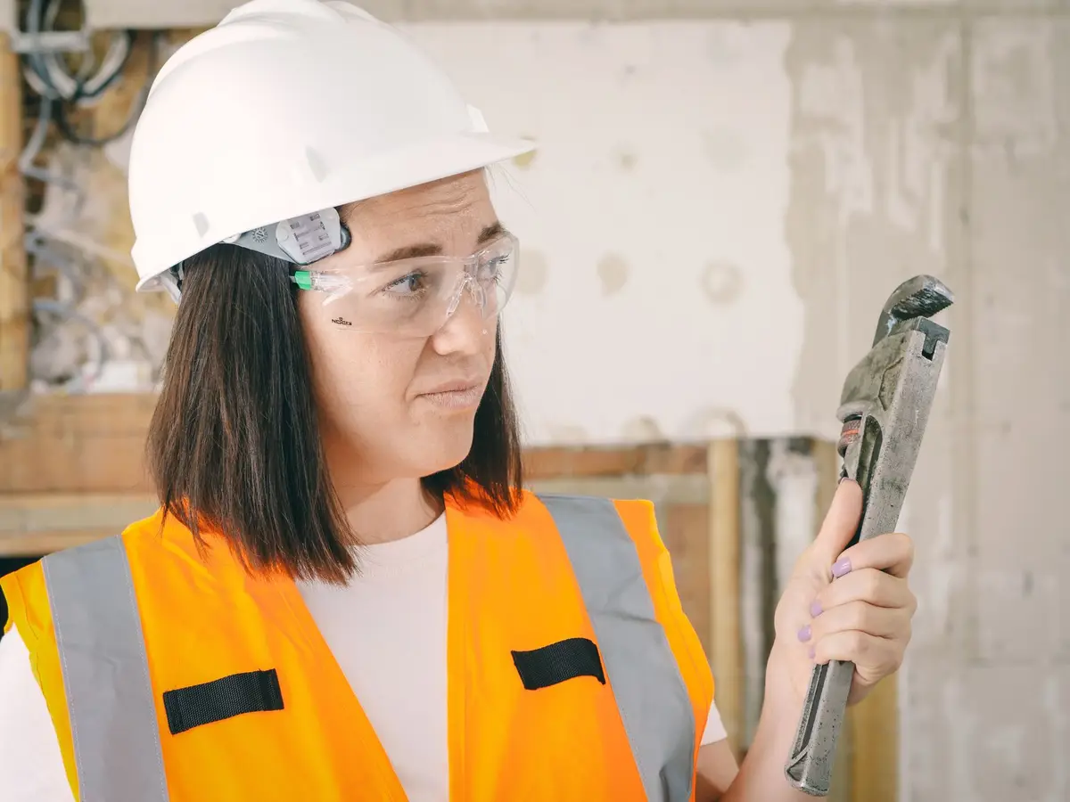A plumber in safety gear holding a pipe wrench on a service call