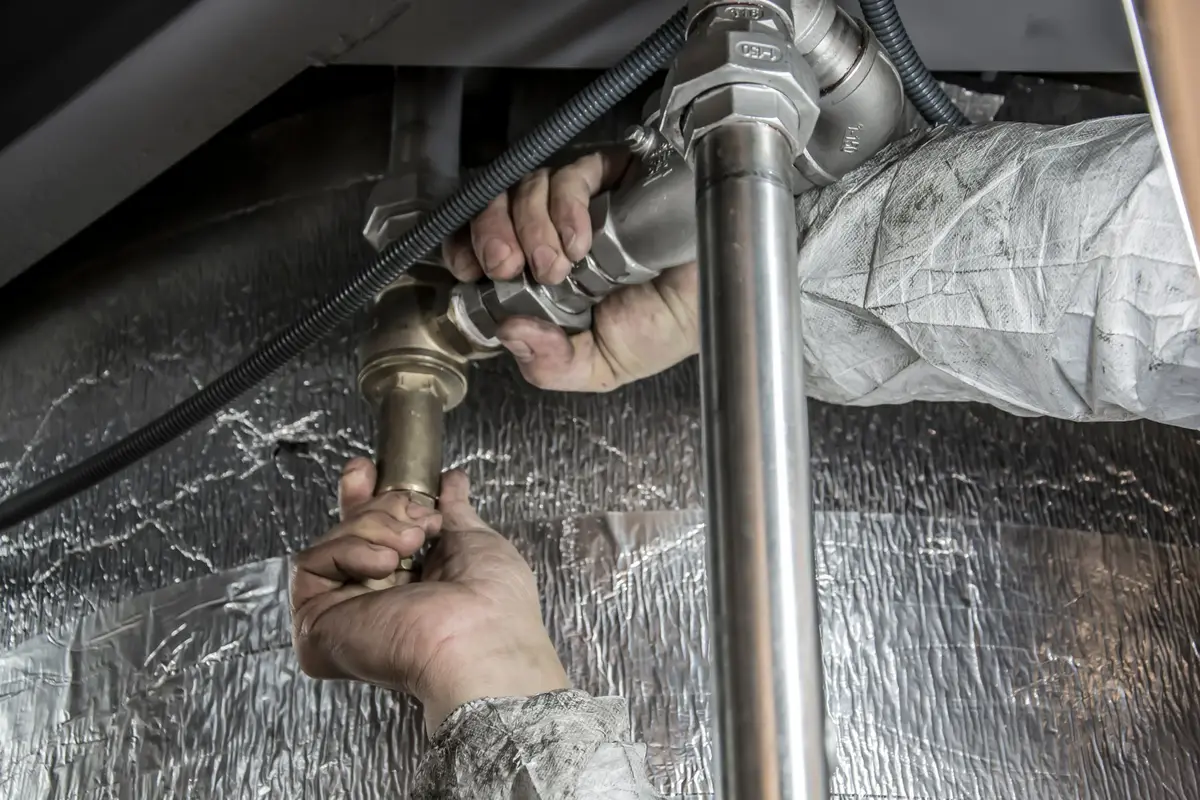 A plumber working overhead on pipes in a tight space