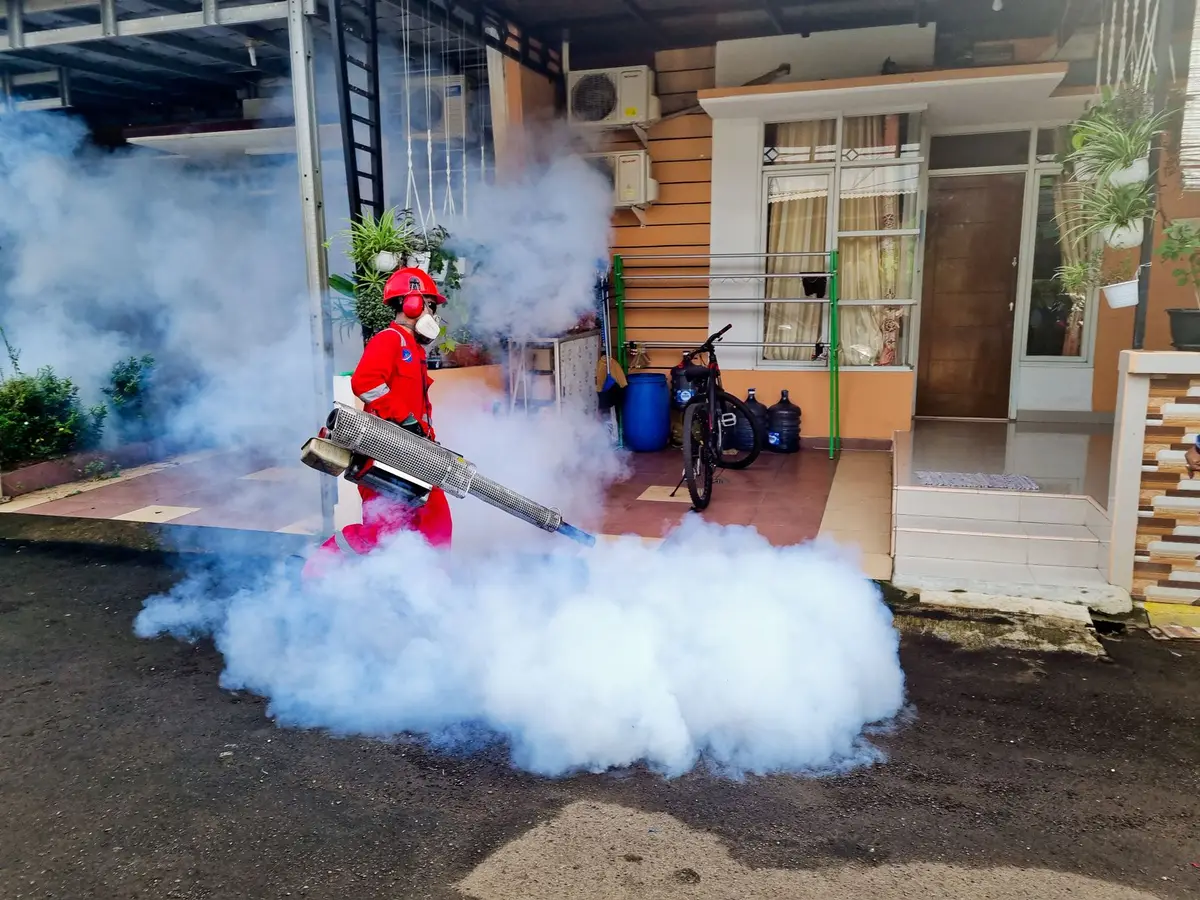 A pest control technician in uniform fogging the exterior of a home