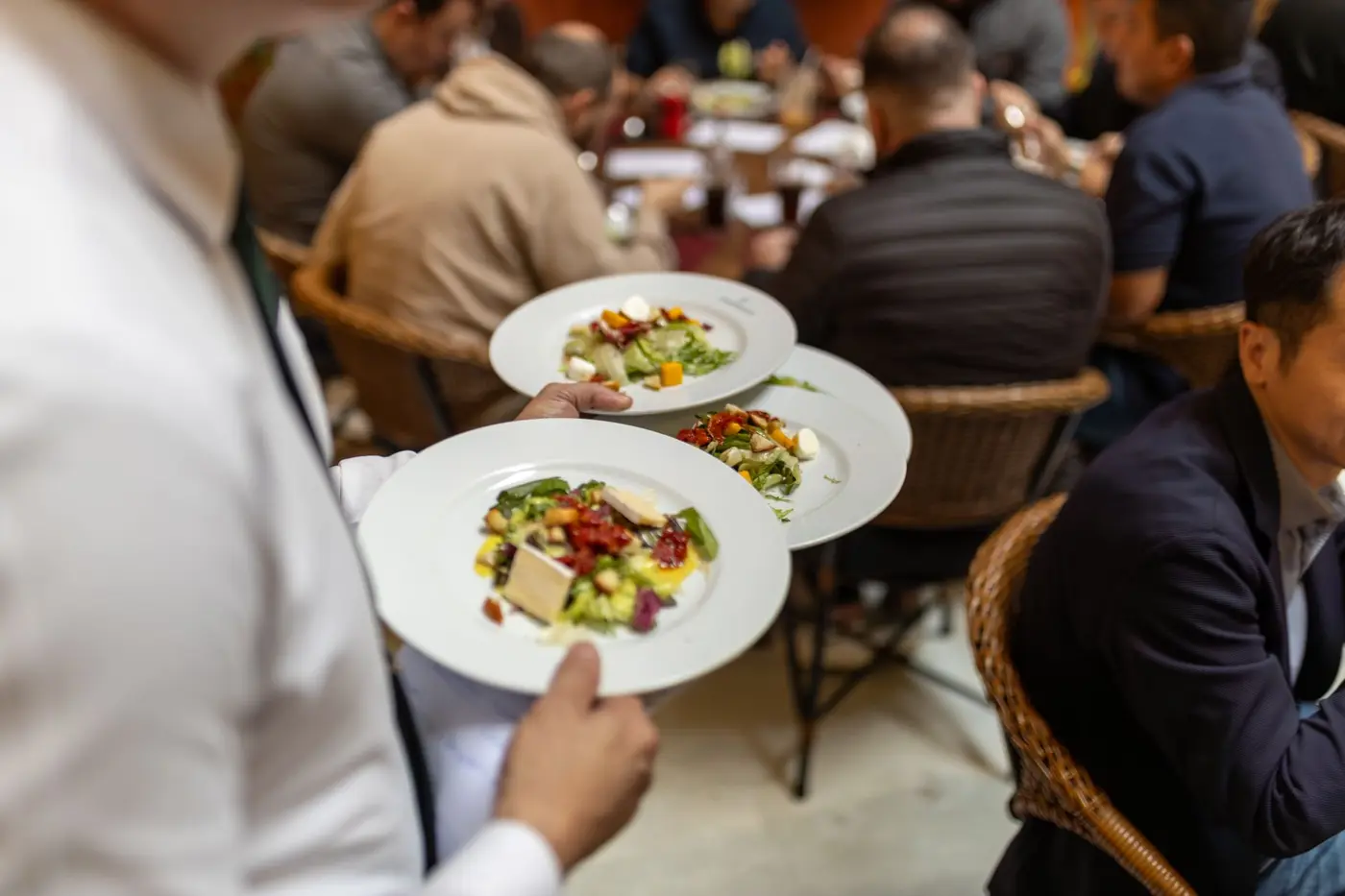 A waiter carrying plates of salad to guests at a restaurant table