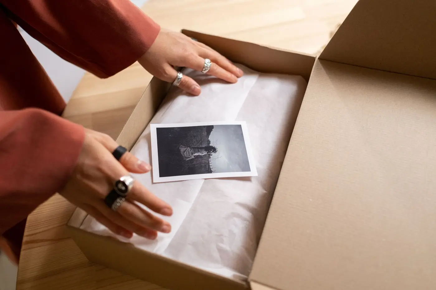 Hands unpacking a cardboard box with tissue paper and a print