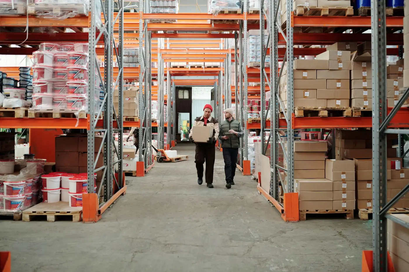 Two warehouse workers handling packages among storage racking