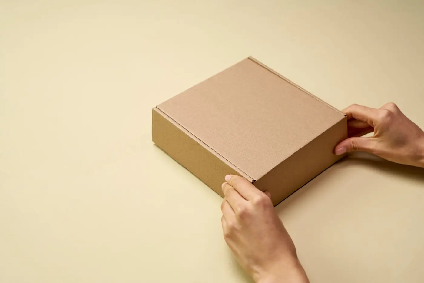 Hands opening a plain kraft cardboard box
