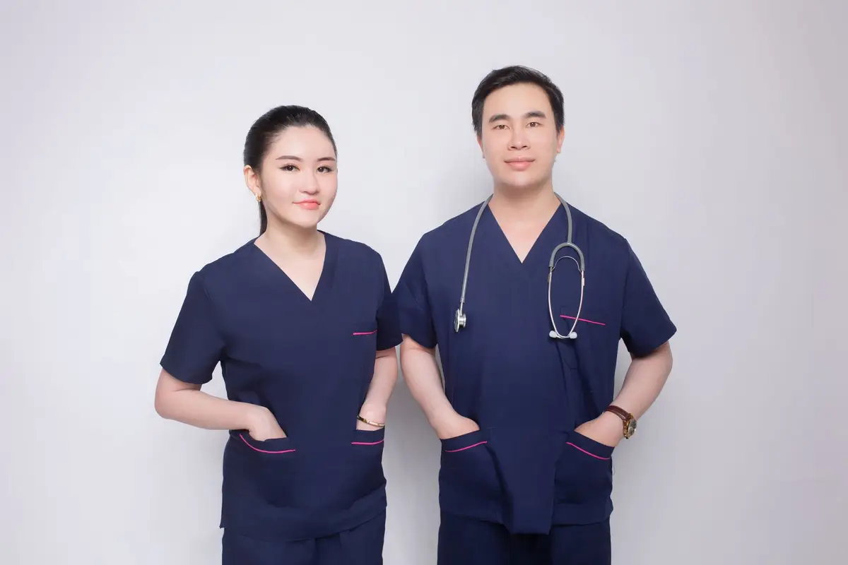 Two medical practitioners in matching navy scrubs with embroidered chest logos