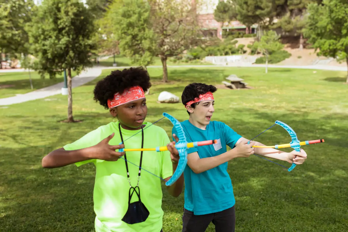 Two campers in bright neon green and teal t-shirts playing with toy bows in a park