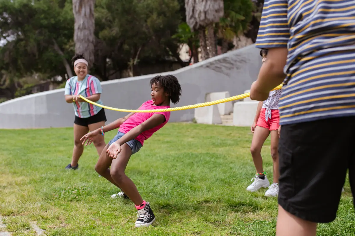 Kids playing a limbo game on the grass at an outdoor summer camp