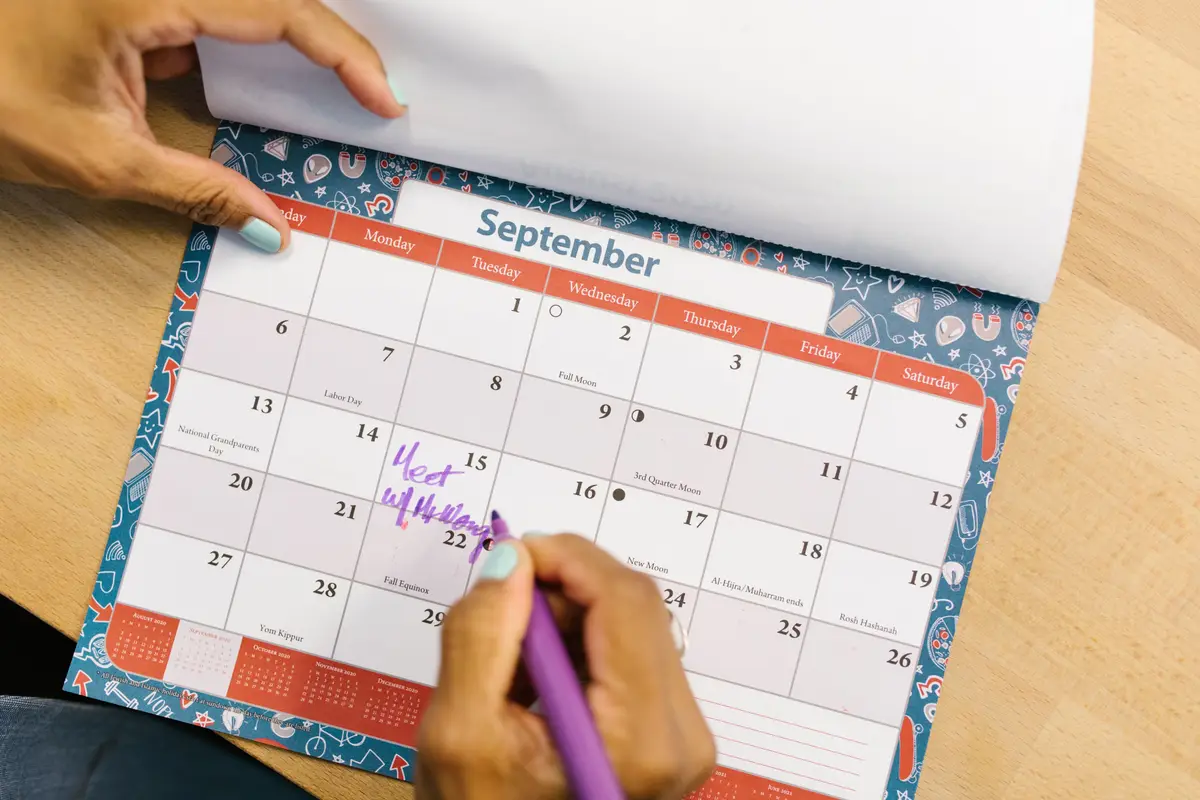 A hand marking dates on a September wall calendar with a purple pen