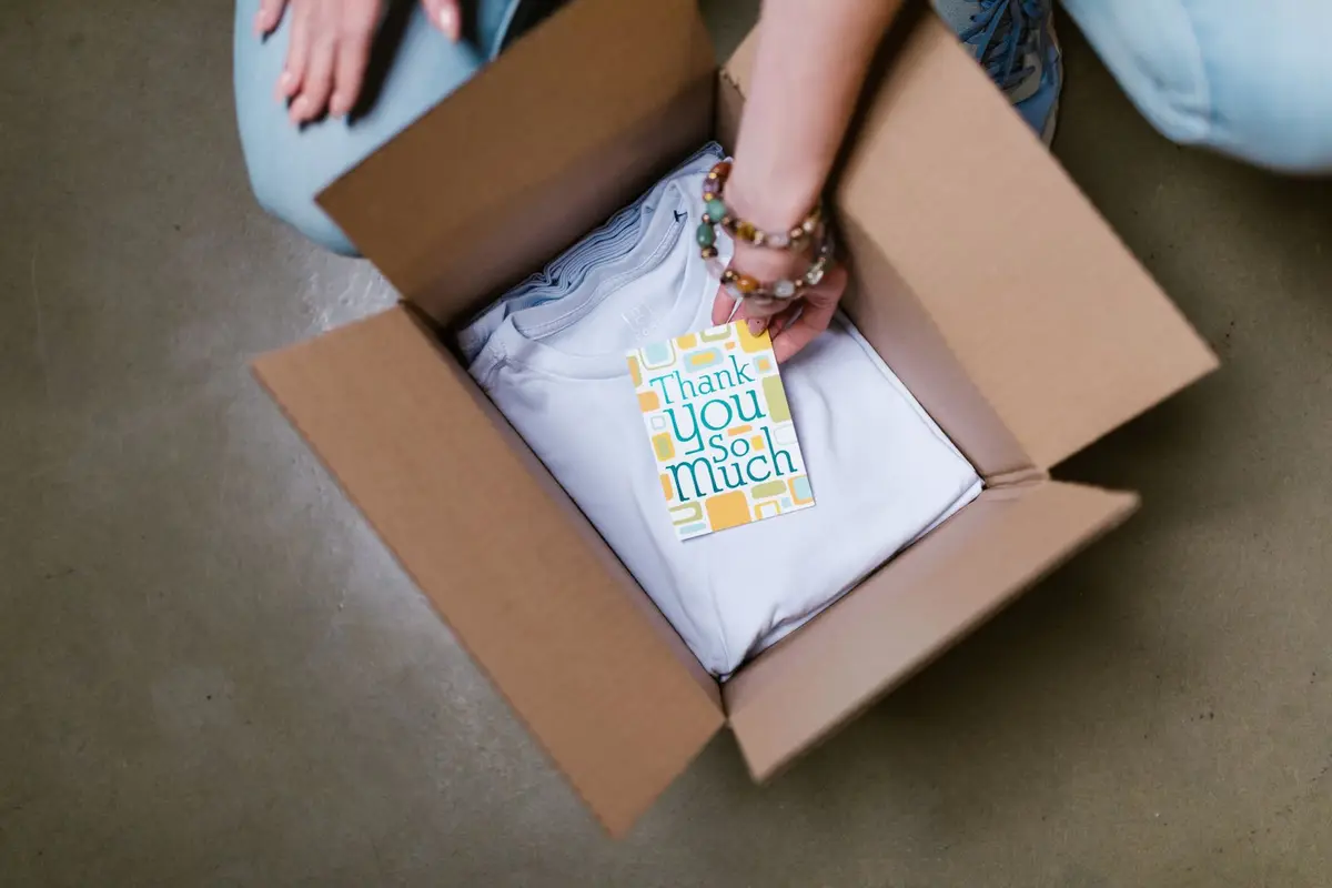 A branded t-shirt and thank-you card being packed into a shipping box
