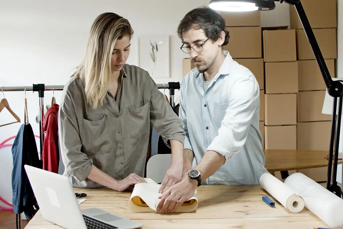 Two people packing apparel orders for shipping in a small workspace